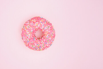 Donut with pink icing and pastry sprinkles on a pink background