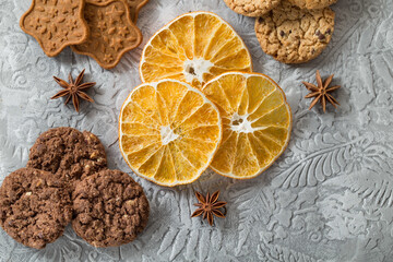 Crispy, aromatic, chocolate and caramel cookies, dried orange slices, anise stars. Stock photo of festive and sweet pastries on a gray textured background.