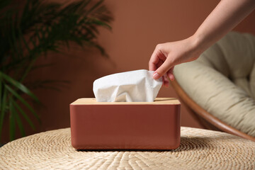 Woman taking paper tissue out of box on table indoors, closeup