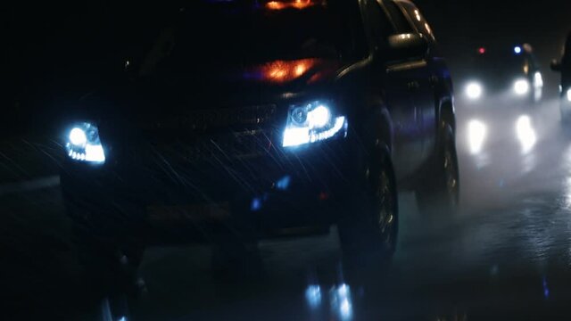 Police SUV driving at high speed in the rain at night. Flashers. The car splashes water from puddles with its wheels.
