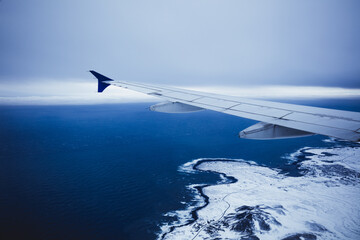 Top view from inside window airplane of a cold atmosphere and wing over Iceland landscape