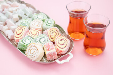 Turkish delight and tea on a metal tray on a pink table.