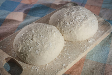 Raw doughs pizza bread with flour on a wooden board on colorful square tablecloth pattern close up view