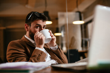 Young businessman working on laptop and drinking coffee in his office. Businessman on coffee break.