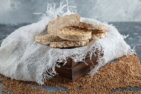 Wooden box of airy crispbread and raw buckwheat on marble surface