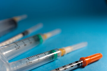 Various types of syringes with caps to protect their needles, seen from a slightly elevated position on a blue background with copy space.