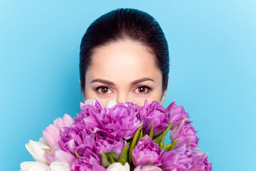 Fototapeta premium Close-up portrait of attractive woman smelling tulips hiding behind bunch isolated over bright blue color background