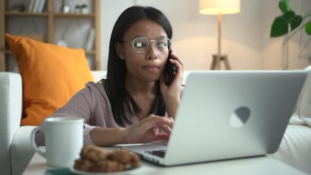 Woman talk on phone and look through laptop Spbd. Communication about work from home living room. African female consult client. Concept email, job, conversation. Millennial tell information