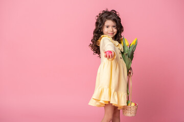 beautiful child girl holding basket with easter eggs and tulips on pink background