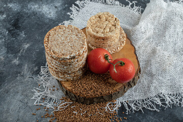 Delicious rice cakes, tomatoes and raw buckwheat on wooden piece