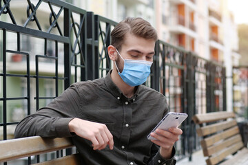 Handsome man in medical protective face mask looks in his smartphone