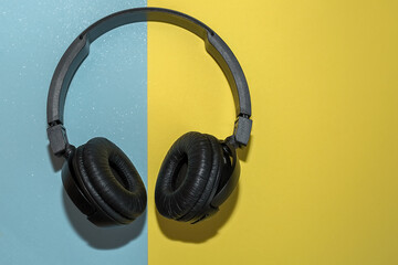 Fototapeta na wymiar Wireless black headphones on a double background of yellow and blue.