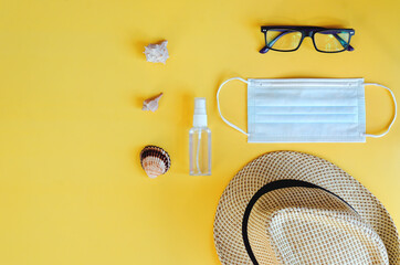 Travel under Covid-19 and new normal concepts. Top view of medical face mask, hand gel sanitizer, glasses and beach hat on yellow background. Creative ideas of prevent coronavirus.