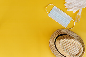 Travel after Covid-19 and new normal concepts. Top view of medical face mask, hand gel sanitizer, gloves and beach hat on yellow background close up. Creative ideas of prevent coronavirus.