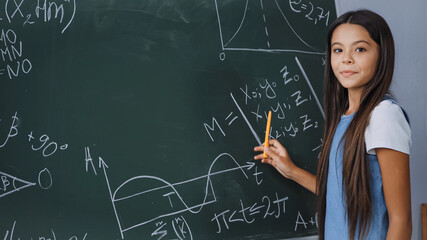 child holding pen while showing mathematical formulas on chalkboard