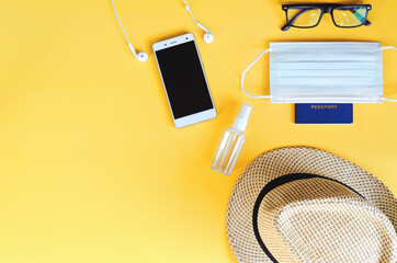 Travel under Covid-19 and new normal concepts. Top view of medical face mask, hand gel sanitizer, passport, headphones  and beach hat on yellow background. Creative ideas of prevent coronavirus.