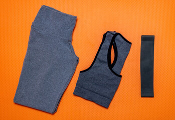 Legging pants with gray top on an orange mat with a black thera band used to exercise at home alone or with friends and family.