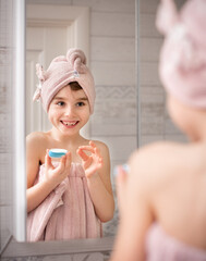 Little beautiful girl in the bathroom. She is holding a cream