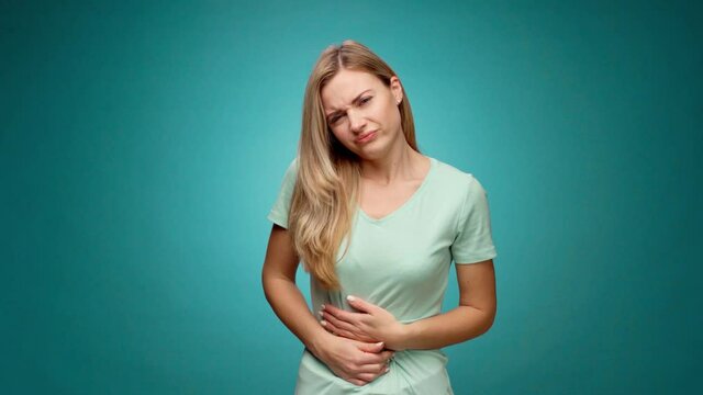 Pretty young woman suffering stomachache, menstruation pain, against mint background