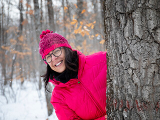 Happy in the snow. In the snowy forest, a woman dressed in mountain clothes, a pink down jacket, gloves and a wool hat, smiles happily in nature.