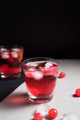Copa de cóctel rojo con cerezas rojas sobre fondo negro y gris