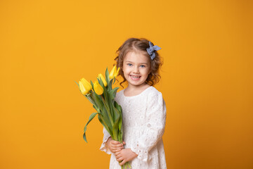 Smiling girl in white dress on yellow background. Cheerful happy child with tulips flower bouquet