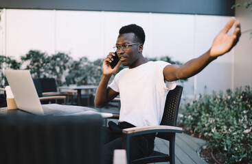 Emotional african american male freelancer gesture discussing software problem with service operator on cellular, stressed dark skinned businessman discussing online project issues on distance job