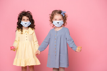 two girls in protective mask with colored eggs holding hands on pink background. Covid easter concept