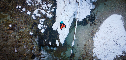 Aerial drone shot of hiker with backpack, orange cap and orange pants next to cold mountain stream in canyon, austria