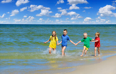 Fototapeta na wymiar Two girls and two boys in colorful t-shirts running on sandy beach
