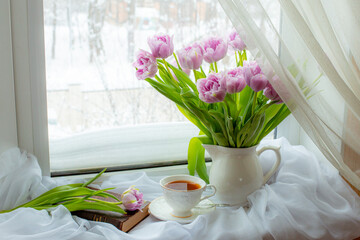 still life a bouquet of lilac tulips in a vase a mug of tea an old book on the window, greeting card with good morning