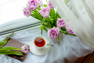 still life a bouquet of lilac tulips in a vase a mug of tea an old book on the window