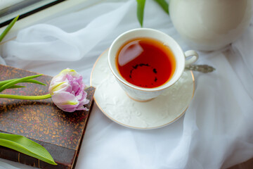 mug of tea an old book a bouquet of tulips on the window