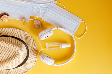 Travel after Covid-19 and new normal concepts. Top view of medical face mask, hand gel sanitizer, headphones and beach hat on yellow background close up. Creative ideas of prevent coronavirus.