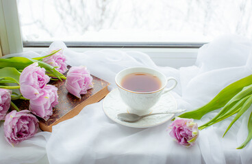 mug of tea an old book a bouquet of tulips on the window