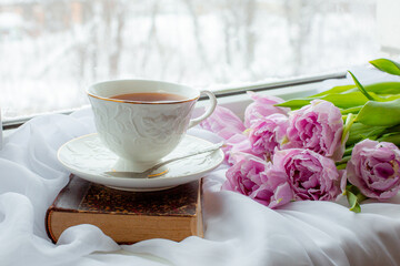 mug of tea an old book a bouquet of tulips on the window