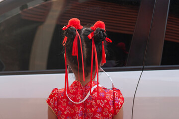 Asian little girl wearing a cheongsam stand back and makes upper two bun hairstyle decorated with...