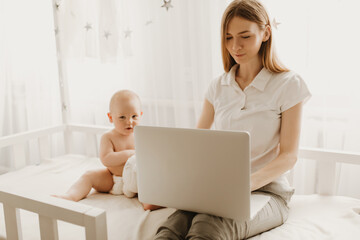 Beautiful young mother works with a laptop and sits with a small child at home