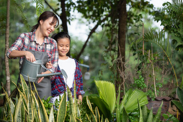 Young Asian mother and daughter happy working in the gardern together on weekend. Daughter helping mother watering.