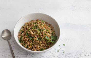 A bowl of vegan buckwheat porridge with herbs and onions on a light gray background. Natural healthy food