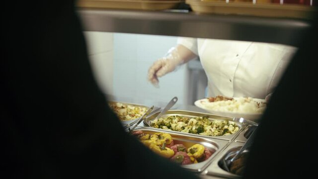 Chef standing behind full lunch service station with assortment of food in trays.