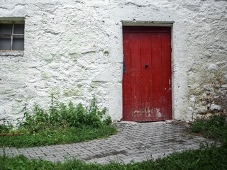 Rote Holztüre in einem alten, grob verputzten Gebäude