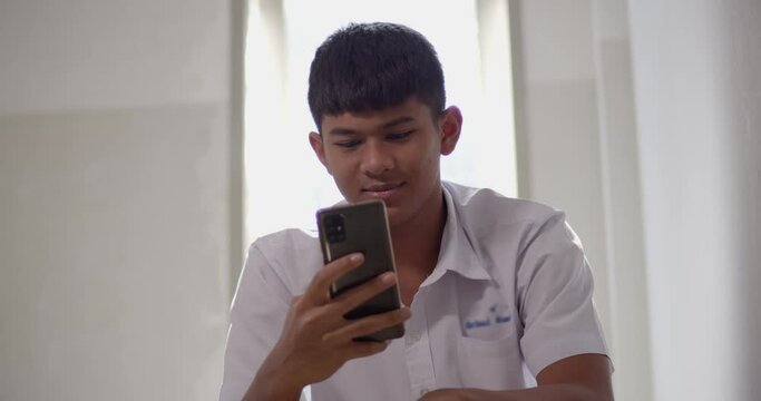 An Asian male high school student in a white school uniform is enjoying a happy smile on his smartphone on the Internet and social media.