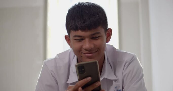 An Asian male high school student in a white school uniform is enjoying a happy smile on his smartphone on the Internet and social media.