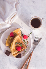 thin homemade pancakes with raspberries and chocolate on a light background on a light plate, with herbs and tea, close-up, vertical arrangement, top view