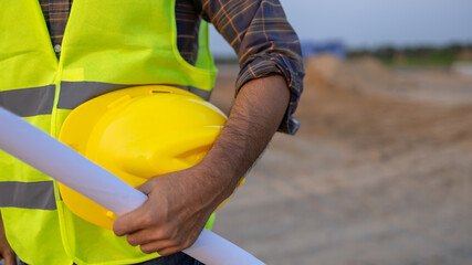 Construction Worker Holding Yellow Hard Hat And Blueprint in Construction Site