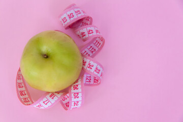 A green apple and a centimeter measuring tape on a pink background. Sports, sports nutrition, healthy eating, diet. Space for the text.