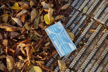 medizinische Maske liegt am Boden neben Herbstlaub