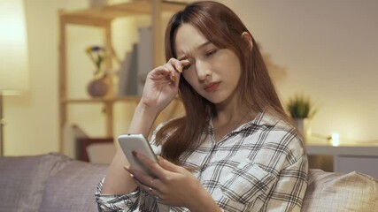 close up Korean young woman having a blurry vision is rubbing and squinting her eyes, trying to see clearly while using cell phone at home.
