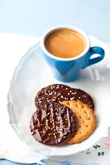 Chocolate cookies with colorful sprinkles and coffee for brunch or breakfast on light blue background, selective focus, close up, copy space. Homemade sweet food. Kids party recipes concept.